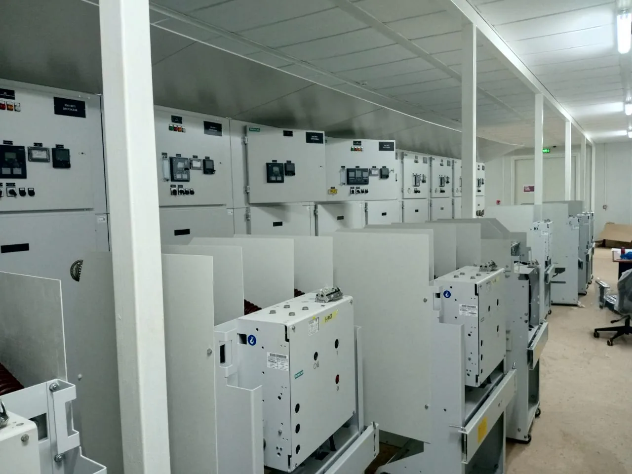 Salle de distribution haute tension : rangée de cellules blindées et disjoncteurs débrochables alignés dans l’allée de manœuvre